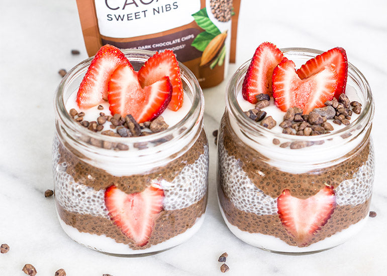 Two mason jars filled with layered chia puddings made with Navitas Organics Chia Seeds and Cacao Powder, topped with fresh sliced strawberries and Navitas Organics Cacao Sweet Nibs
