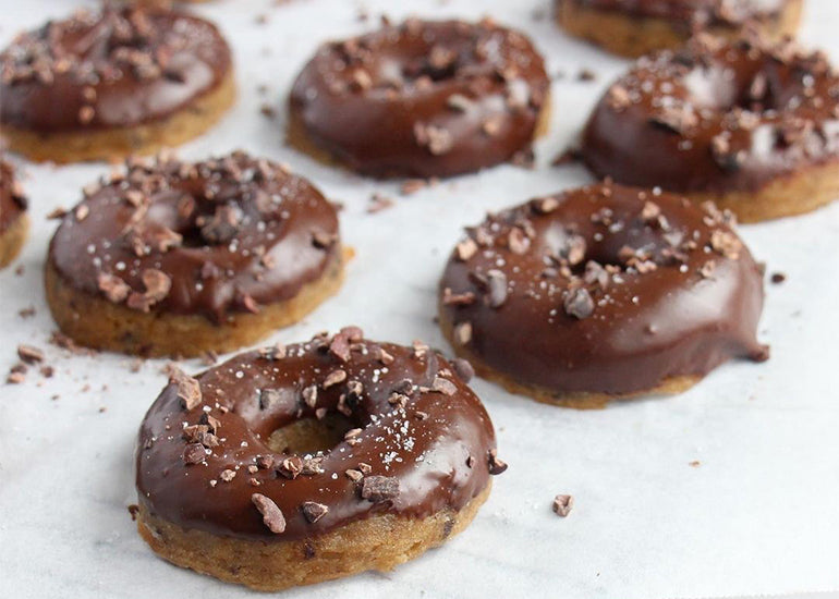 Rows of chocolate peanut butter glazed donuts topped with Navitas Organics Cacao Nibs
