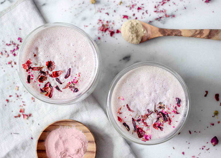 Two pink lattes made with Navitas Organics Cashew Nuts, Pomegranate Powder and Gelatinized Maca Powder, topped with dried rose petals