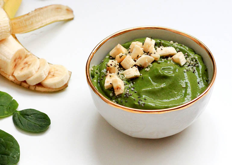 A green smoothie bowl made with Navitas Organics Wheatgrass Powder and Vanilla & Greens Essential Blend, topped with banana slices and Navitas Organics Chia Seeds