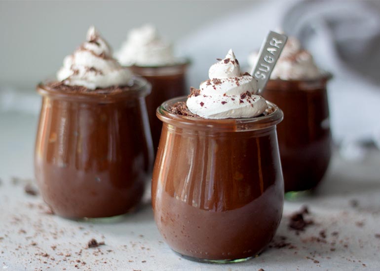 Three serving glasses filled with chocolate avocado pudding made with Navitas Organics Cacao Powder, topped with whipped cream and shaved chocolate