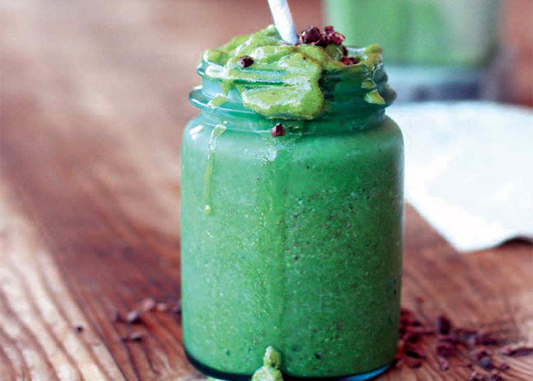 A mason jar overflowing with a green smoothie made with Navitas Organics Cashews and Cacao Sweet Nibs