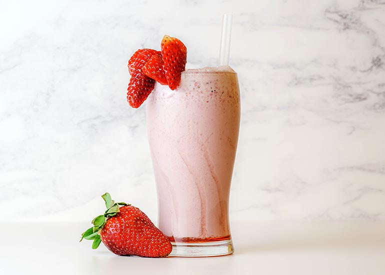 A tall glass filled with a pink smoothie made with Navitas Organics Goji Berry Powder and Camu Powder, garnished with fresh strawberries