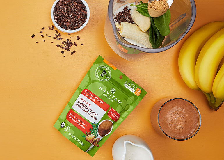 A smoothie made with Navitas Organics Superfood+ Adaptogen Blend, surrounded by Navitas Organics Cacao Nibs and bananas
