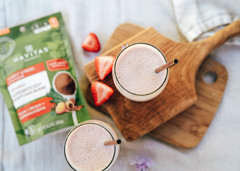Two strawberry banana cream smoothies made with Navitas Organics Superfood+ Adaptogen Blend and Chia Seeds on wooden boards with fresh strawberries