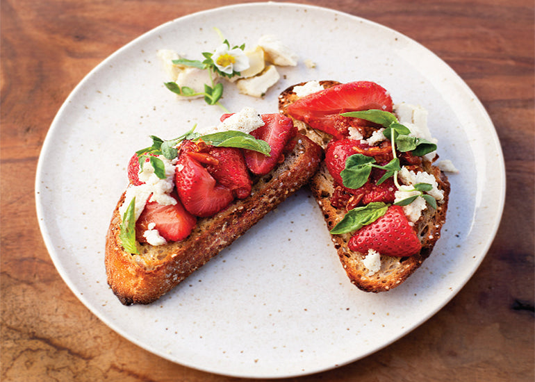 Two slices of toast topped with fresh strawberries, nut cheese, basil and Navitas Organics Goldenberries