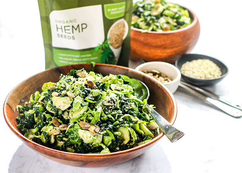 A bowl of kale and Brussels salad mixed with Navitas Organics Hemp Seeds, topped with a tahini dressing