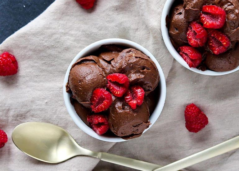 Two dishes filled with super berry chocolate mousse made with Navitas Organics Superfood+ Berry Blend, Cacao+ Antioxidant Blend, and Cacao Powder, topped with fresh raspberries