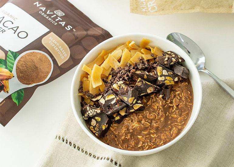 A nutty chocolate oatmeal bowl made with Navitas Organics Cacao Powder and Cacao Nibs, topped with nutty chocolate bark and coconut shavings.