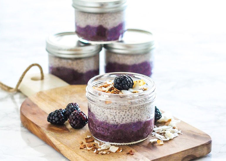 Mason jars filled with acai coconut chia parfaits made with Navitas Organics Acai Powder and Chia Seeds, topped with blackberries and toasted coconut flakes. 