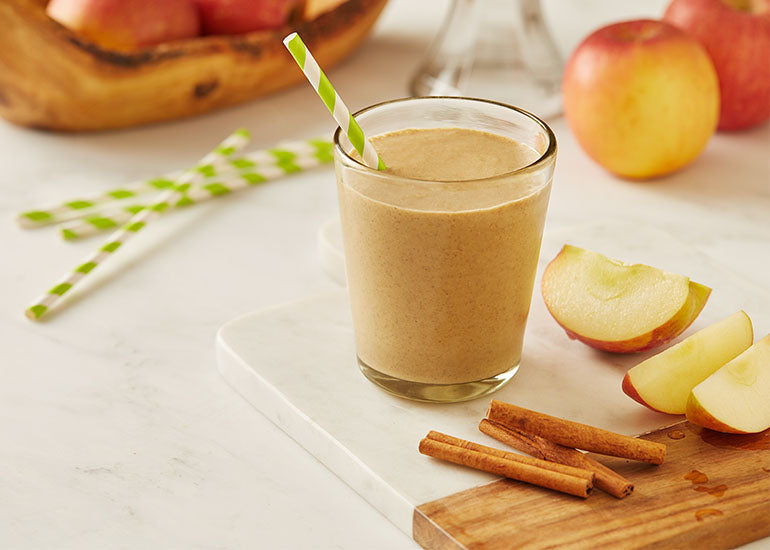 A smoothie made with Navitas Organics Hemp Powder in a serving glass next to sliced apples and cinnamon sticks.
