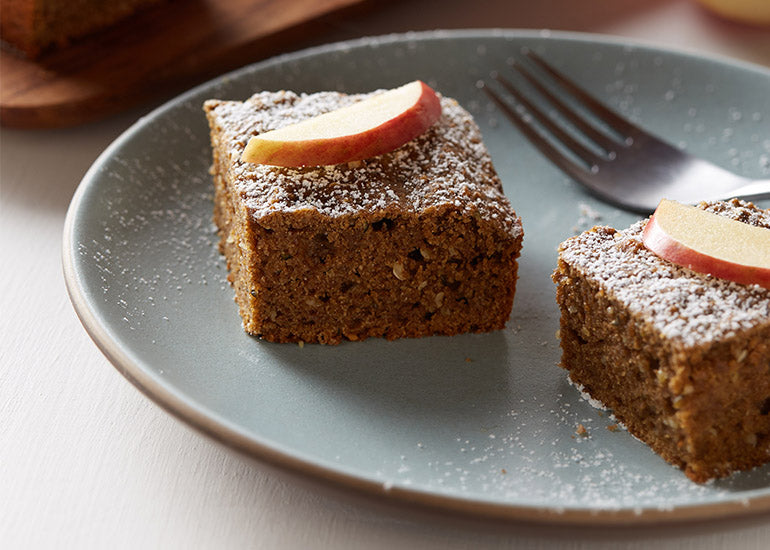 A plate with two pieces of applesauce cake made with Navitas Organics Hemp Powder and Hemp Seeds, topped with fresh apple slices.