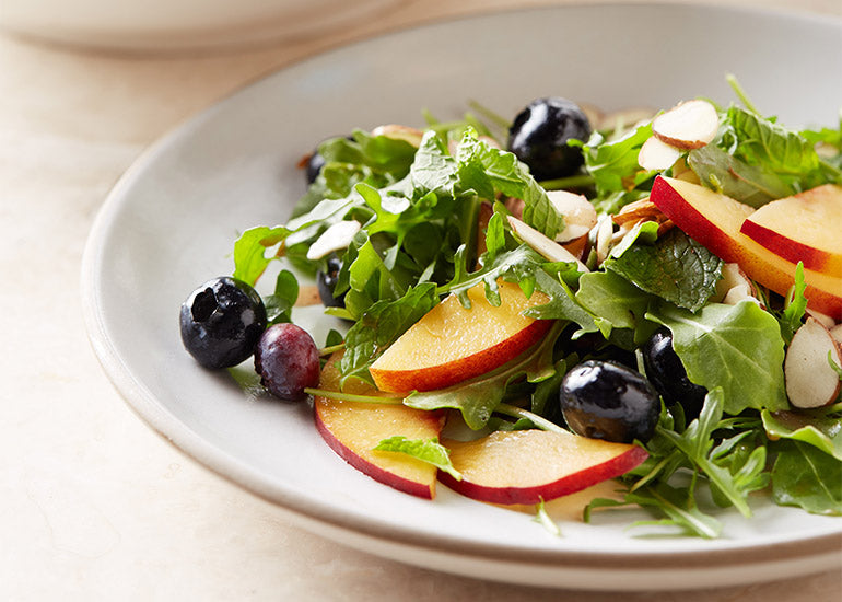 A plate of arugula salad with blueberries and peaches, topped with a dressing made with Navitas Organics Pomegranate Powder.