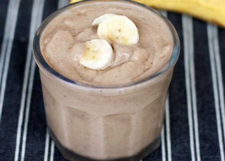 A glass filled with a banana smoothie made with Navitas Organics Mulberries, topped with fresh banana slices.