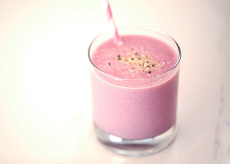 A glass filled with a pink smoothie made with Navitas Organics Goji Berries, Maqui Powder, Acai Powder and Hemp Seeds, topped with hemp seeds.