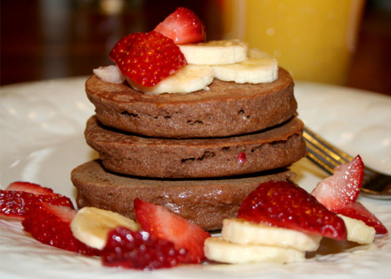 A stack of blueberry acai buckwheat pancakes made with Navitas Organics Acai Powder, topped with fresh fruit.