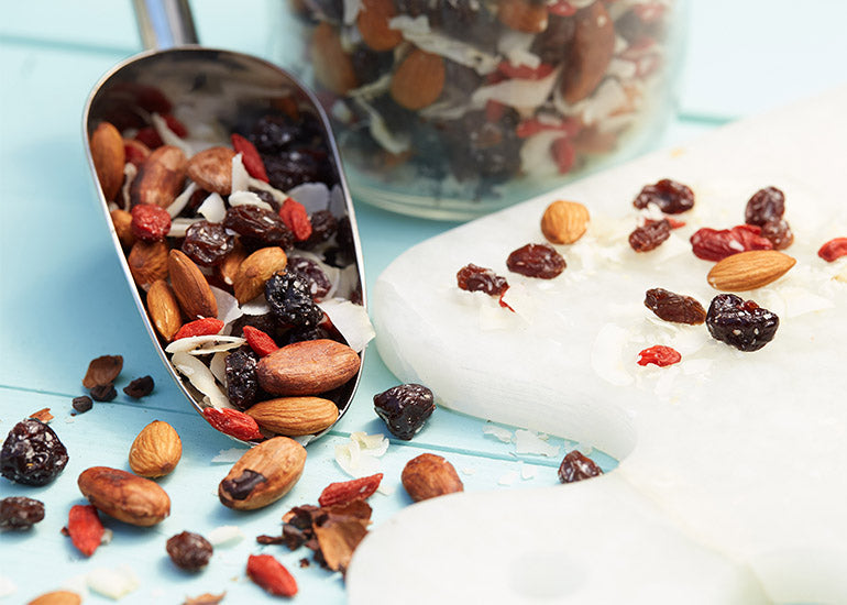 A large scoop filled with healthy superfood trail mix made with Navitas Organics Goji Berries and Cacao Nibs.