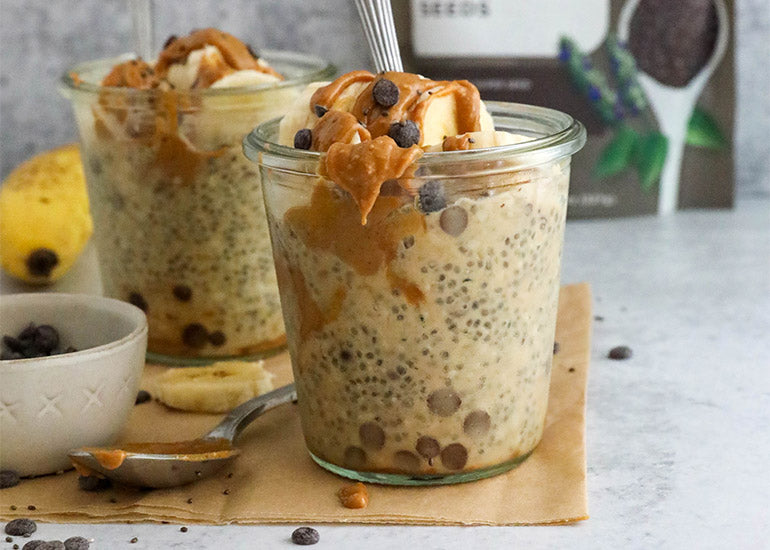 Two glass jars filled with peanut butter and banana chocolate chip chia pudding, made with Navitas Organics Chia Seeds, Hemp Seeds and Cacao Nibs.