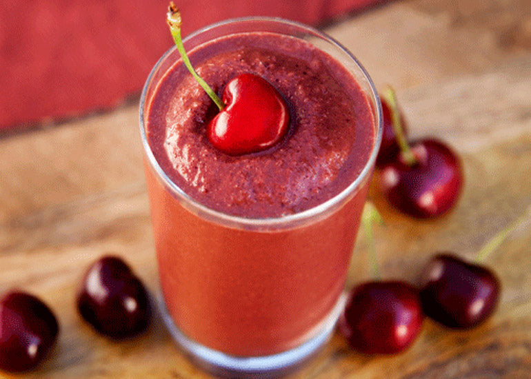 A glass filled with a bright red smoothie made with Navitas Organics Cashew Nuts, Goji Berries and Superfood+ Berry Blend, topped with a fresh cherry.