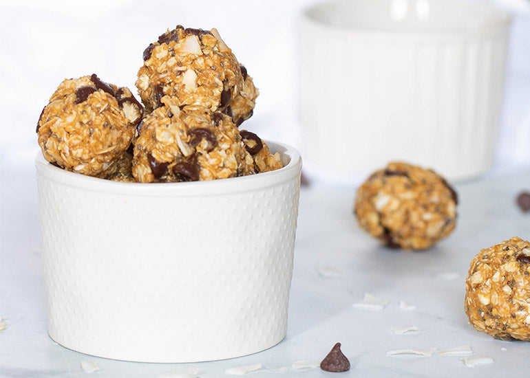 A white ceramic container overflowing with chocolate coconut energy bites made with Navitas Organics Chia Seeds.