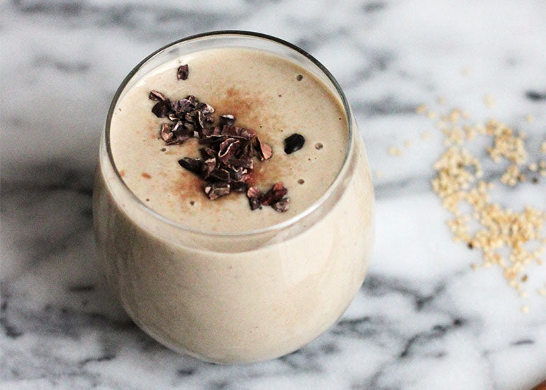 A glass filled with a chocolate smoothie made with Navitas Organics Cacao Powder and Maca Powder, topped with Navitas Organics Cacao Nibs.