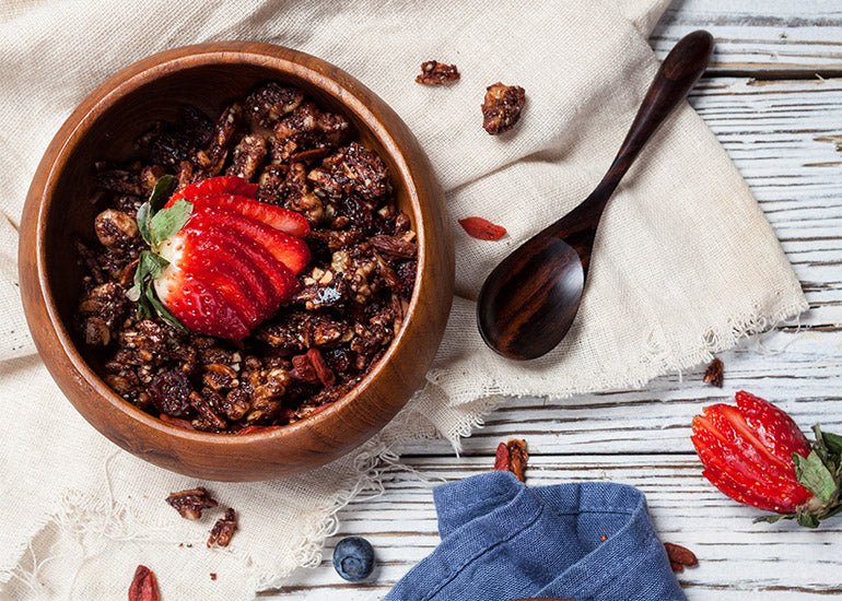 A wooden bowl filled with chocolate goji granola made with Navitas Organics Cacao Powder, Chia Seeds and Goji Berries, topped with fresh strawberries.
