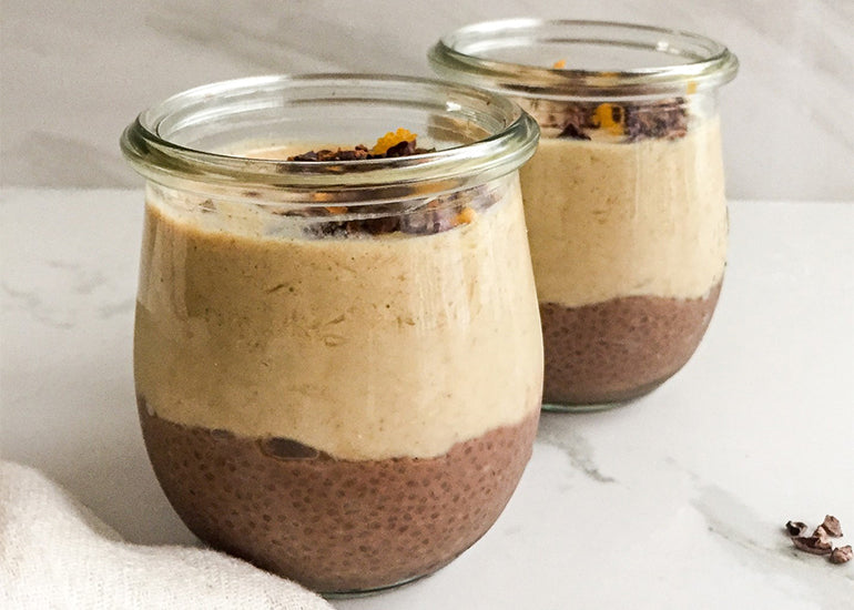 Two glass cups filled with chocolate orange chia pudding made with Navitas Organics Chia Seeds, Cacao Powder and Superfood+ Immunity Blend, topped with Navitas Organics Cacao Nibs
