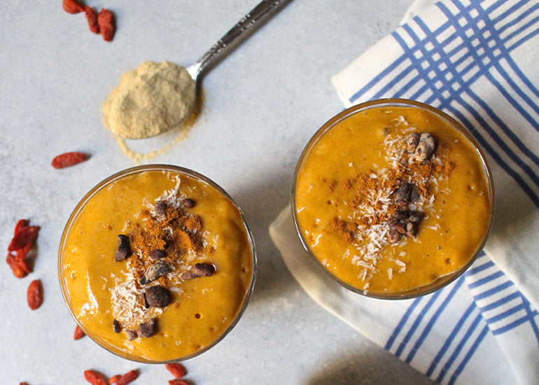 Two orange smoothies made with Navitas Organics Superfood+ Immunity Blend and Goji Berries, topped with Cacao Nibs.