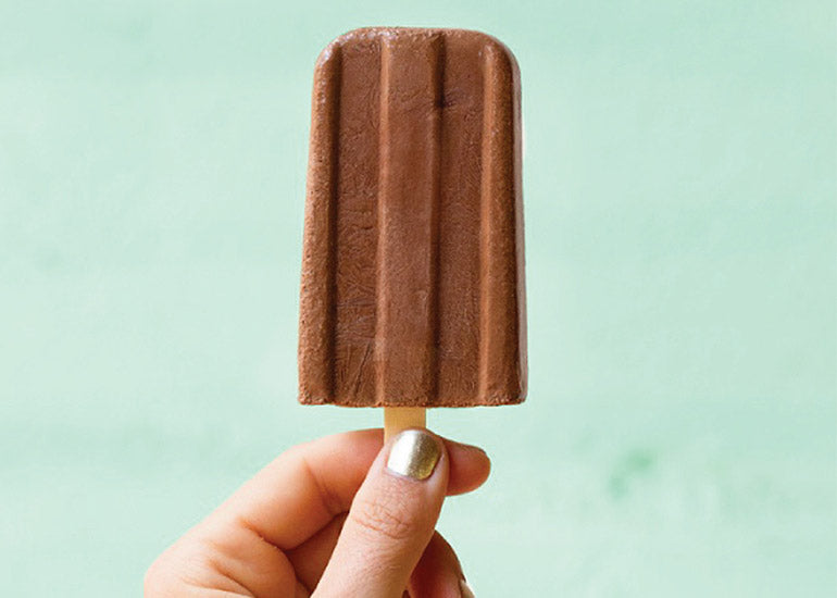 A woman holding a fudge popsicle made with Navitas Organics Cacao Powder and Maca Powder.
