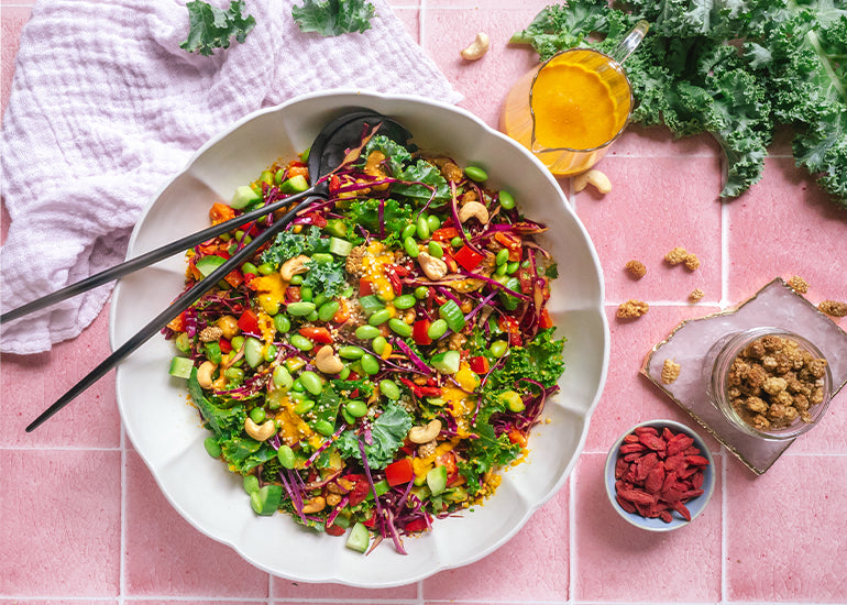 A bowl of kale salad with carrot ginger dressing made with Navitas Organics Goji Berries, Mulberries, Hemp Seeds and Turmeric Powder.