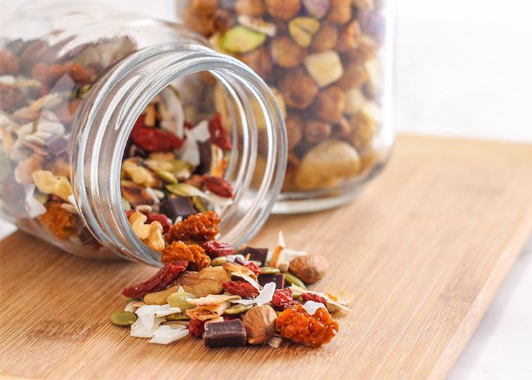 A mason jar on filled with superfood trail mix made with Navitas Organics Goji Berries and Goldenberries on its side, spilling out onto a cutting board.