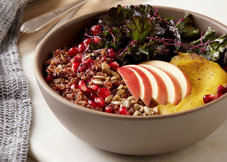 A bowl filled with quinoa, squash, kale and other healthy ingredients, mixed with Navitas Organics Pomegranate Powder.