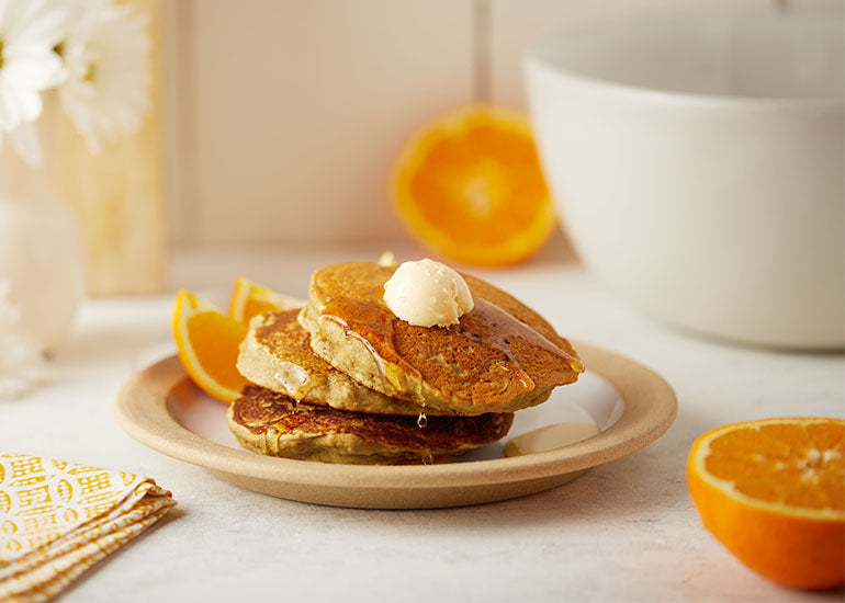 A plate of pancakes made with Navitas Organics Superfood+ Immunity Blend, topped with syrup and served with orange slices.