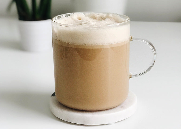 A glass mug filled with a creamy, frothy keto cacao butter coffee made with Navitas Organics Cacao Butter Wafers.