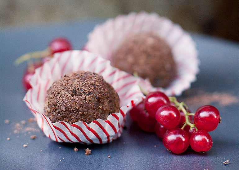 Two truffles made with Navitas Organics Gelatinized Maca Powder and Cacao Sweet Nibs, wrapped in festive paper.
