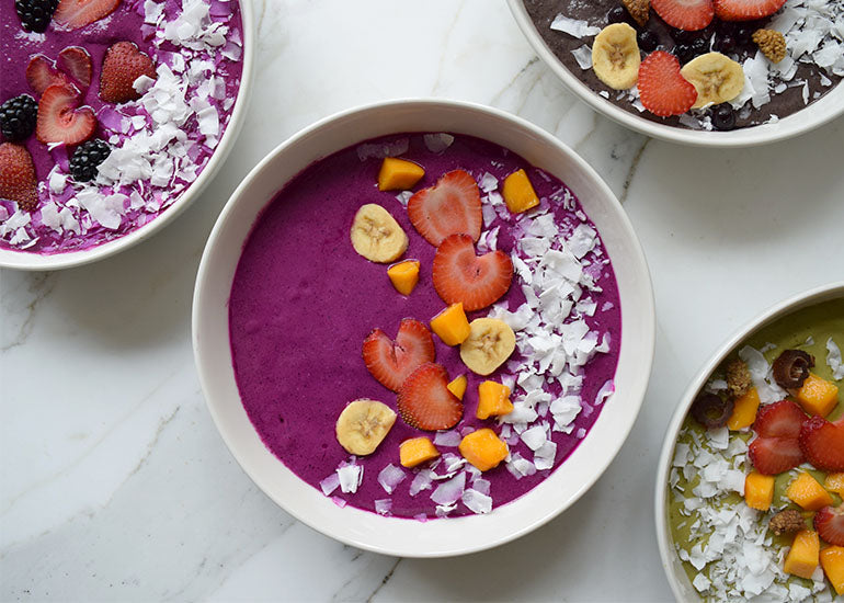 Pink pitaya smoothie bowls made with Navitas Organics Hemp Seeds, Chia Seeds and Maca Powder, topped with fresh fruit and coconut.