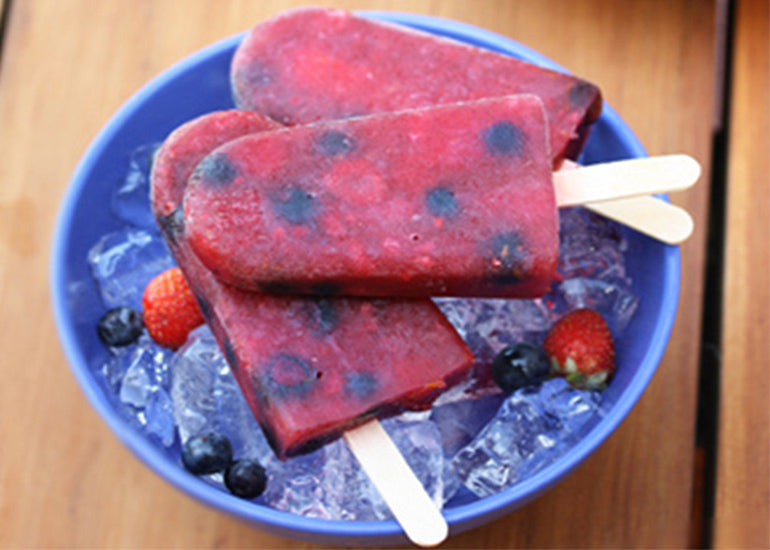 A bowl filled with ice and strawberries topped with frozen popsicles made with Navitas Organics Pomegranate Powder.