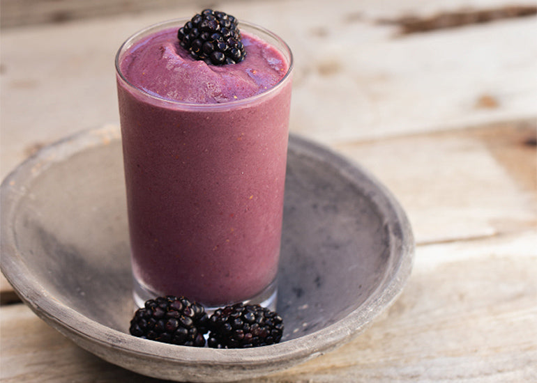 A tall glass filled with a rich purple smoothie made with Navitas Organics Chia Seeds and Pomegranate Powder, topped with a fresh blackberry.