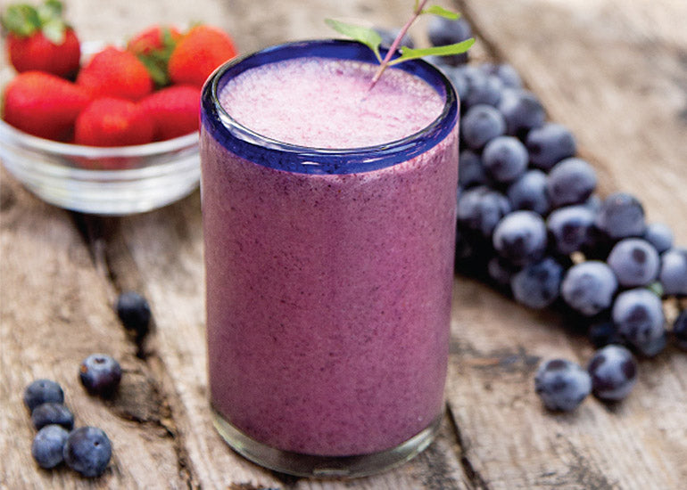 A glass filled with a deep purple berry smoothie made with Navitas Organics Superfood+ Berry Blend.