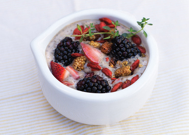 A bowl filled with a superfood breakfast mix, made with Navitas Organics Hemp Seeds, Maca Powder and Chia Seeds, topped with fresh fruit, and Navitas Organics Goji Berries and Mulberries.