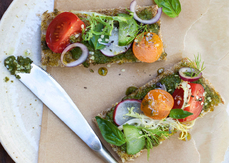 Two slices of whole grain bread topped with a pesto sauce made with Navitas Organics Hemp Seeds, veggies, and more Hemp Seeds.