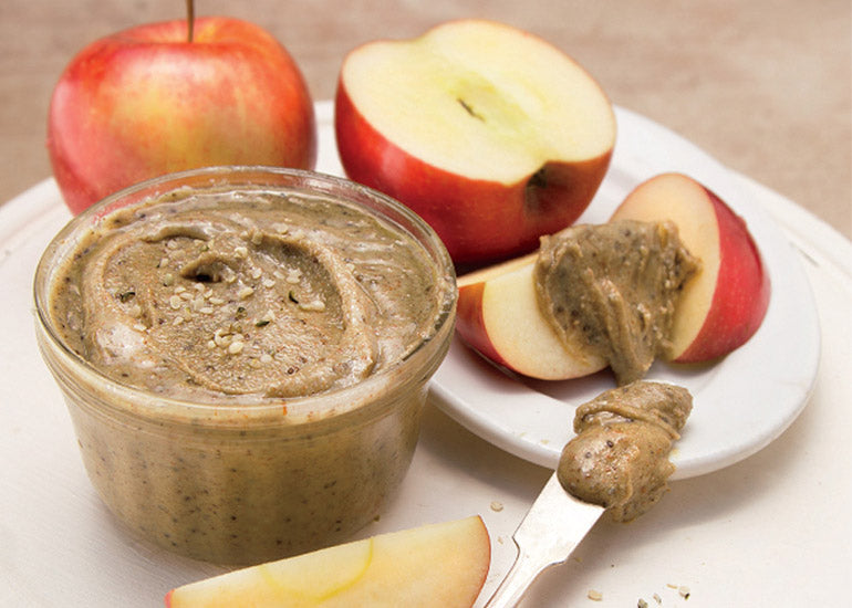 A jar of power seed nut butter made with Navitas Organics Hemp Seeds and Chia Seeds, alongside sliced apples.