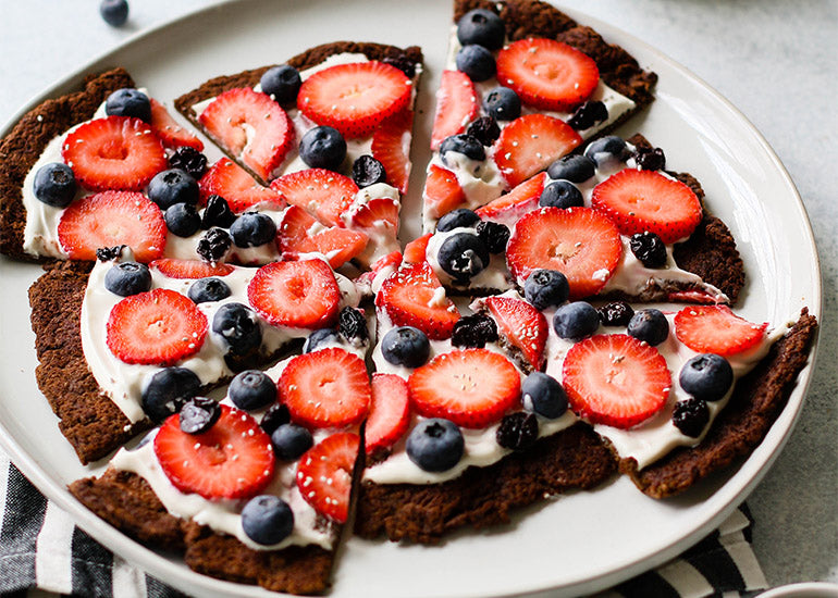 A chocolate protein-rich sweet pizza made with Navitas Organics Cacao Powder, topped with yogurt, berries, Navitas Organics Chia Seeds and Cacao Nibs