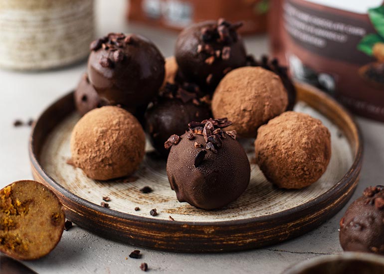 A plate of pumpkin-spiced cake balls made with Navitas Organics Cacao Powder and Cacao Wafers, coated and topped with Navitas Organics Cacao Nibs and Cacao Sweet Nibs.