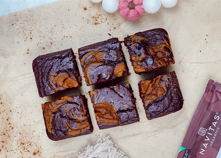Six chocolate pumpkin swirl brownies made with Navitas Organics Cacao Powder on parchment paper.