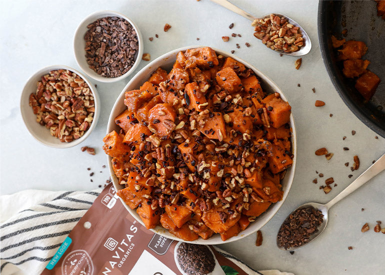 A bowl of candied yams topped with Navitas Organics Cacao Nibs and pecans.