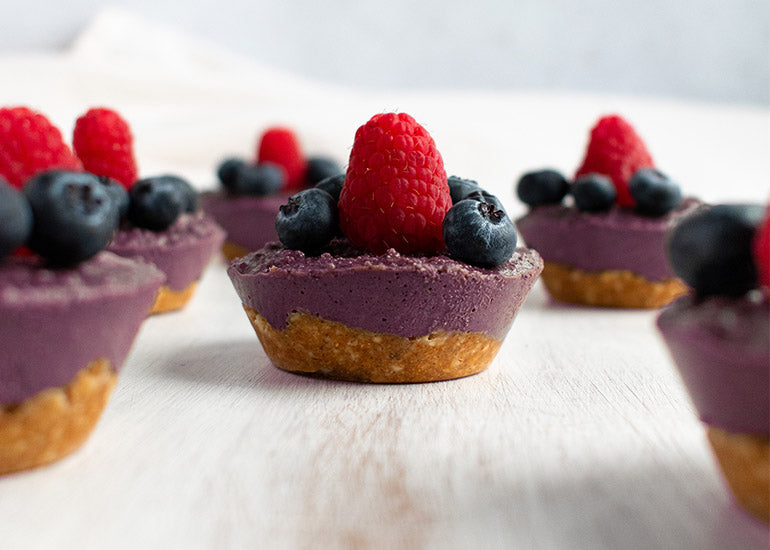 Mini vegan acai cheesecakes made with Navitas Organics Chickpea Flour and Acai Powder, topped with fresh berries.
