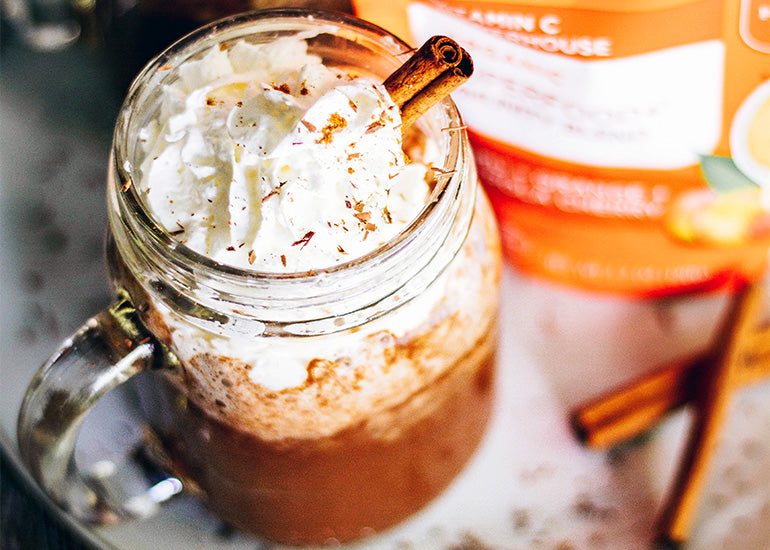 A mason jar filled with hot cocoa made with Navitas Organics Cacao Powder and Superfood+ Immunity Blend, topped with whipped cream and cinnamon