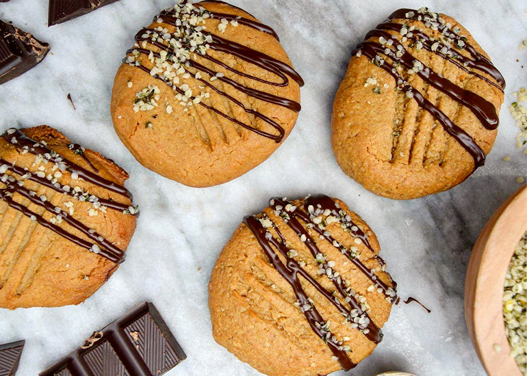 Peanut butter maca cookies made with Navitas Organics Maca Powder, drizzled with chocolate and sprinkled with Navitas Organics Hemp Seeds.