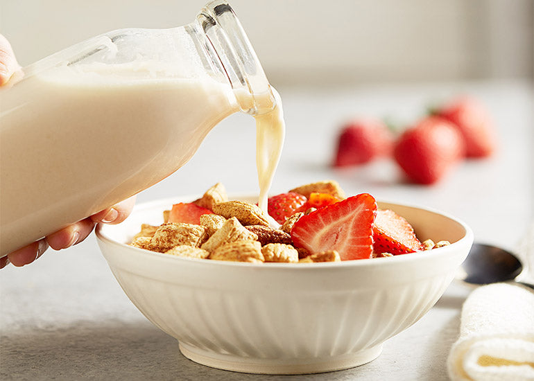 A woman pouring milk made with Navitas Organics Hemp Seeds into a bowl of cereal topped with fresh strawberry slices.